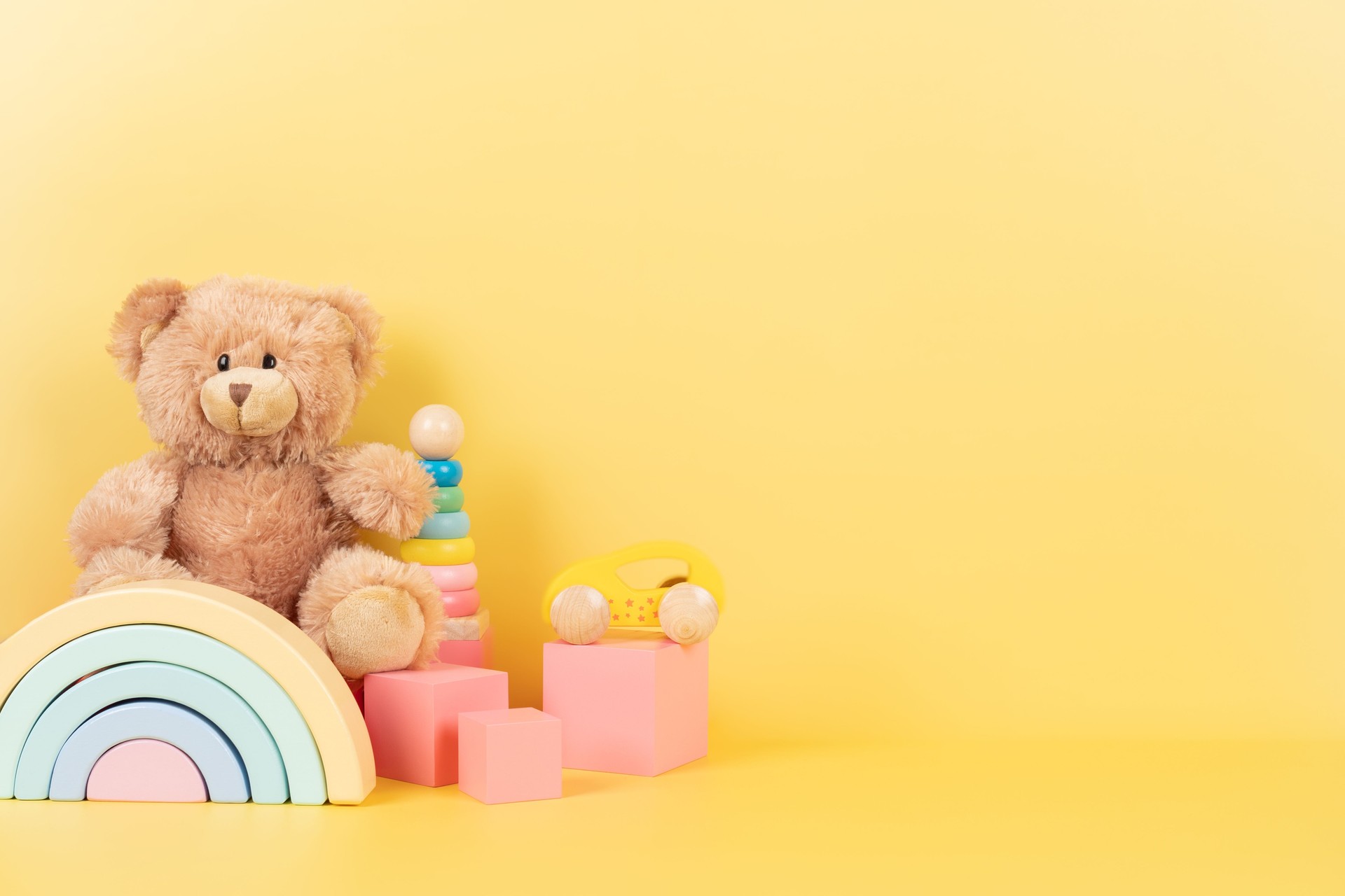 Educational kids toys collection. Teddy bear, wooden rainbow pink cubes and colorful balls on yellow background. Front view
